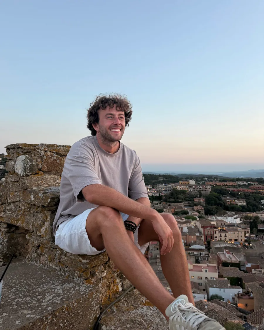 Martin, souriant, assis sur un vieux mur de pierre au coucher du soleil.